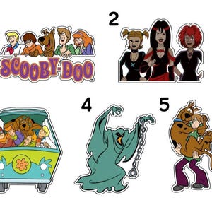 May include: A collection of cartoon stickers featuring characters and elements from the Scooby-Doo franchise. Includes the Scooby-Doo gang, the Mystery Machine van, and various villains. The stickers are colorful and have a cartoon style.