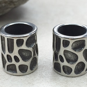 May include: Two silver metal beads with a textured, organic pattern. The beads are cylindrical and have a smooth, polished finish.