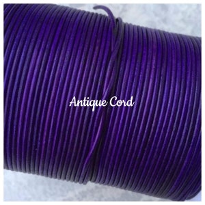 May include: A close-up of a spool of deep purple leather cord. The cord is smooth and has a slight sheen. The text "Antique Cord" is printed on the spool.