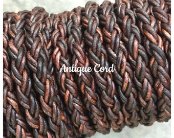 May include: Close-up of a braided leather cord in brown and copper tones. The cord is tightly woven and has a rustic, antique look. The text "Antique Cord" is visible on the cord.
