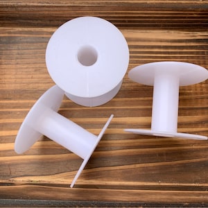 May include: Three white plastic spools for thread or yarn. The spools have a large flat base and a smaller round center hole.