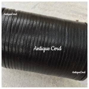 May include: Close-up of black leather cord, rolled up. The cord is smooth and has a subtle texture. The text "Antique Cord" is visible on the cord.