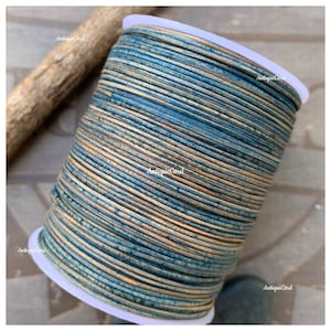 May include: A spool of blue and tan cord with the text "AntiqueCord" printed on the side. The cord is tightly wound on a white plastic spool. A piece of wood is in the background.