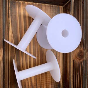 May include: Three white plastic spools with a center hole for thread. The spools are in a wooden box.