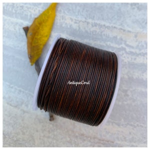 May include: A spool of dark brown leather cord, wound tightly on a white plastic spool. The cord is smooth and has a slightly textured surface. The text "AntiqueCord" is printed on the spool.