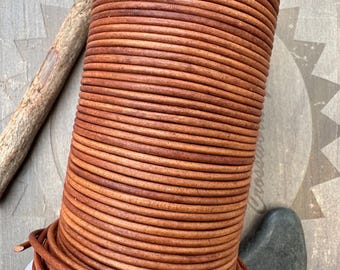 May include: A spool of brown leather cord, wound tightly in a coil. The cord is smooth and has a natural, rustic look.