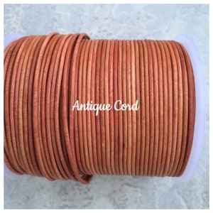 May include: A spool of orange leather cord, wound tightly. The cord is smooth and has a slightly textured surface. The label on the spool reads "Antique Cord".