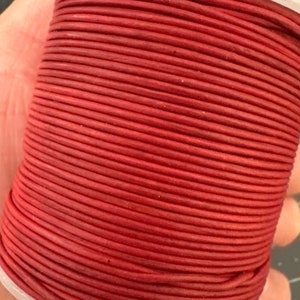 May include: A spool of red leather cord. The cord is tightly wound around a white plastic core. The color of the cord is a deep, rich red, and the texture appears smooth. This cord is suitable for various crafting projects.