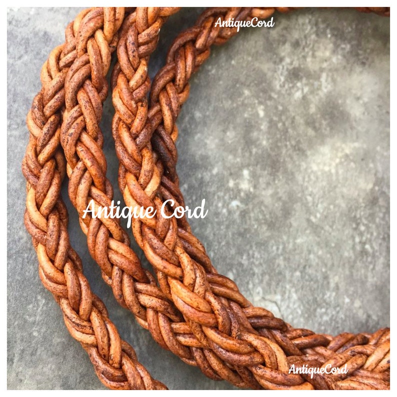 May include: Close-up of a thick, braided leather cord in a brown color. The cord is woven with a tight, intricate pattern. The cord is on a textured surface. The text "Antique Cord" appears twice in the image.