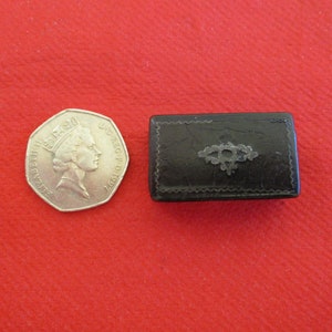 May include: A small black leather box with a silver design on the top. The box is about the size of a 20 pence coin.
