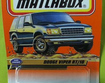 May include: A blue Matchbox Dodge Viper RT/10 die-cast toy car with black wheels and a black interior. The car is on a plastic blister pack with a white background. The packaging has the words "Matchbox", "Dodge Viper RT/10", and "Car Shows" printed on it. The car is number 37 of 100 vehicles.