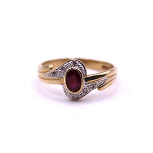 Pode incluir: Um anel de ouro com uma pedra preciosa de rubi oval no centro, rodeada por pequenas pedras claras. O anel tem um design de haste dividida e está sobre um fundo branco.
