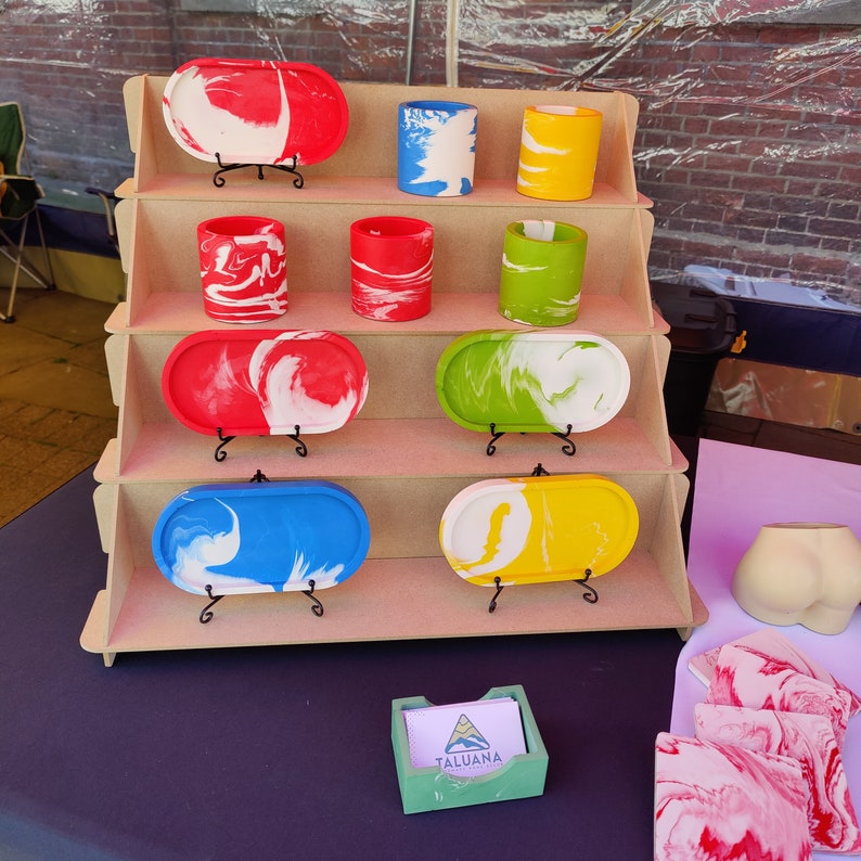 Matching pen pots and pill-shaped trays in all four colours on a display stand at a market stall. Some Taluana-branded business cards are in the foreground, in a sage green business card holder.