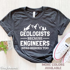 May include: A dark gray t-shirt with a white graphic design of mountains and the text "Geologists - Because - Engineers Need Heroes Too".