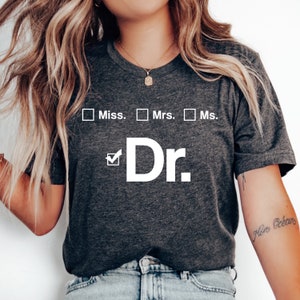 May include: A dark gray t-shirt with a white graphic that says "Miss., Mrs., Ms. Dr." with a checkmark next to the "Dr."