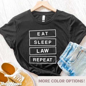May include: Black t-shirt with white text that reads "Eat Sleep Law Repeat".