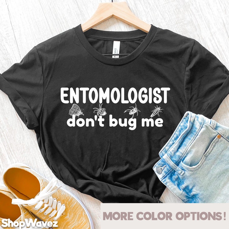 May include: Black t-shirt with the text "ENTOMOLOGIST don't bug me" in white. The shirt features insect illustrations. A pair of blue denim shorts and yellow sneakers are visible.