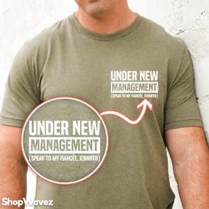 May include: A green t-shirt with the text "UNDER NEW MANAGEMENT (SPEAK TO MY FIANCÉE, JENNIFER)" printed on it.