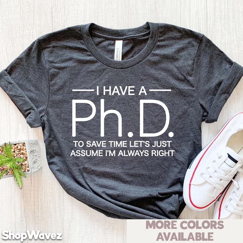 May include: A dark gray t-shirt with white text that reads "I have a Ph.D. To save time let's just assume I'm always right".