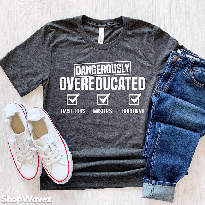 Peut inclure: Un t-shirt gris fonc&eacute; avec le texte "Dangerously Overeducated" et une liste de contr&ocirc;le avec des coches &agrave; c&ocirc;t&eacute; de "Bachelor's", "Master's" et "Doctorate".