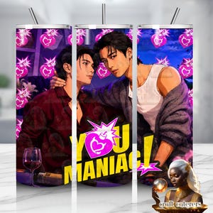 May include: A cylindrical metal tumbler featuring a graphic illustration of two individuals in a close embrace. The design includes a repeating pattern of pink heart-shaped bomb icons and the bold yellow text "YOU MANIAC!" with a pink starburst accent.
