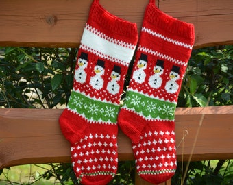 May include: Two red and white knitted Christmas stockings with a snowman pattern. The stockings are hanging on a wooden fence.