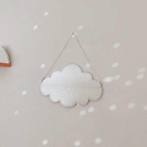 Könnte beinhalten: Ein silberner, wolkenförmiger Spiegel mit einer Perlenbordüre hängt an einer silbernen Kette an einer hellbeigen Wand. Der Spiegel reflektiert das Licht eines Fensters und erzeugt ein Muster aus weißen Kreisen an der Wand.