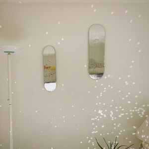 Puede incluir: Dos espejos rectangulares con un dise&ntilde;o de azulejos espejados cuelgan de una pared blanca. Los espejos est&aacute;n colocados verticalmente y est&aacute;n ligeramente desplazados uno del otro. La pared est&aacute; cubierta de peque&ntilde;os puntos redondos blancos.
