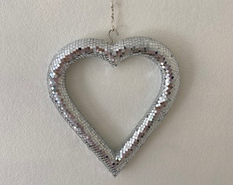 May include: A silver heart-shaped decoration with a mirrored finish, hanging from a silver chain.