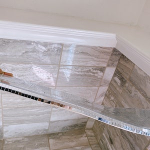 Puede incluir: Un borde de azulejos de espejo plateado se est&aacute; instalando en un ba&ntilde;o con azulejos de m&aacute;rmol gris claro.