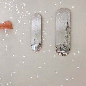 Puede incluir: Dos espejos ovalados plateados con un dise&ntilde;o de mosaico est&aacute;n montados en una pared de color beige claro. La pared tiene un patr&oacute;n de peque&ntilde;os puntos blancos.