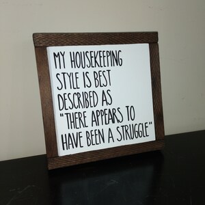 Puede incluir: Un letrero de madera con el texto "MY HOUSEKEEPING STYLE IS BEST DESCRIBED AS "THERE APPEARS TO HAVE BEEN A STRUGGLE""