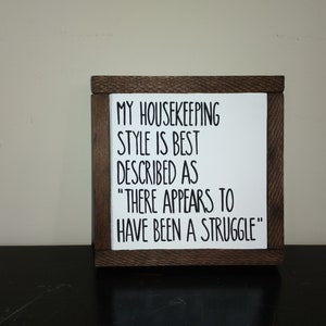 Puede incluir: Un letrero de madera con el texto "MY HOUSEKEEPING STYLE IS BEST DESCRIBED AS "THERE APPEARS TO HAVE BEEN A STRUGGLE""