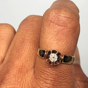 May include: A gold ring with a single round diamond set in a floral design. The ring is worn on a finger.