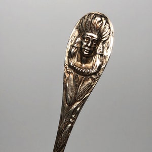 May include: Silver spoon with an ornate handle featuring a Native American chief's head in profile, surrounded by corn stalks.
