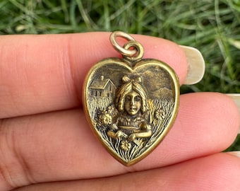 Puede incluir: Colgante vintage en forma de corazón con un relieve detallado. El colgante presenta una joven rodeada de flores y una casa al fondo. El colgante es de metal dorado y tiene un lazo para una cadena.