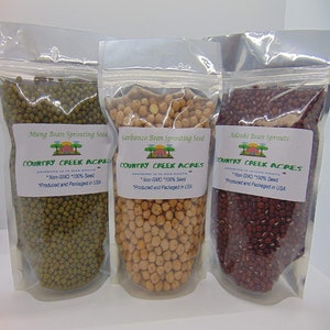 May include: Three clear plastic bags filled with different types of sprouting seeds. The bags are labeled "Mung Bean Sprouting Seed", "Garbanzo Bean Sprouting Seed", and "Adzuki Bean Sprouts". Each bag has a label with the company name "Country Creek Acres" and the text "*Non-GMO 100% Seed *Produced and Packaged in USA".