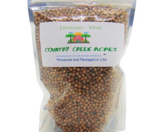 Könnte beinhalten: Ein durchsichtiger Plastikbeutel gefüllt mit ganzen Koriandersamen. Der Beutel trägt ein Etikett mit der Aufschrift "Coriander - Whole" und "COUNTRY CREEK ACRES" mit dem Slogan "GROWING IS IN OUR ROOTS." Das Etikett trägt außerdem den Hinweis "*Produced and Packaged in USA."