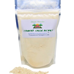 May include: A clear plastic bag filled with light beige onion powder. The bag has a white label with the text "Onion Powder" and "COUNTRY CREEK ACRES". A small pile of onion powder sits in front of the bag. The text "Growing is in our roots" is also visible.