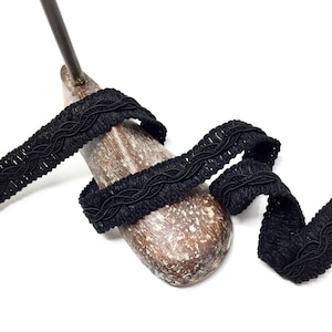 May include: Black braided trim with a woven design. The trim is displayed on a wooden spool.