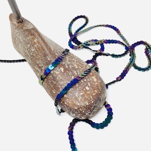 May include: A strand of iridescent blue and green sequins on a black thread. The sequins are arranged in a continuous line and are wrapped around a wooden shoe form.