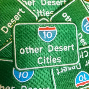 May include: Green embroidered patches with white text and a blue and red highway sign with the number 10. The text on the patches reads "other Desert Cities".