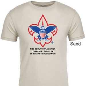Könnte beinhalten: Ein sandfarbenes T-Shirt mit dem Logo der Boy Scouts of America, das einen rot-weiß-blauen Adler mit einem Schild zeigt. Der Text unter dem Logo lautet "BOY SCOUTS OF AMERICA", "Troop 914 Dallas, Tx" und "St. Luke "Community" UMC".