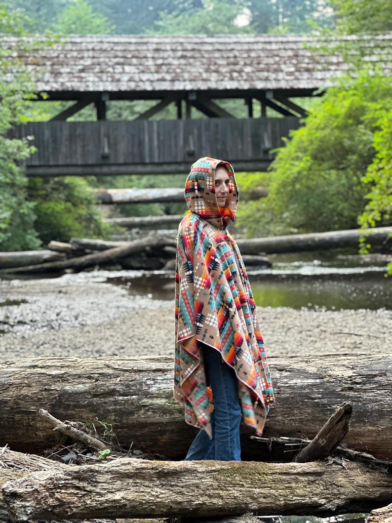 Puede incluir: Una persona lleva una capucha con un patr&oacute;n geom&eacute;trico colorido. La capucha es marr&oacute;n, naranja, roja, azul y blanca. La persona est&aacute; de pie en un entorno boscoso con un puente de madera en el fondo.