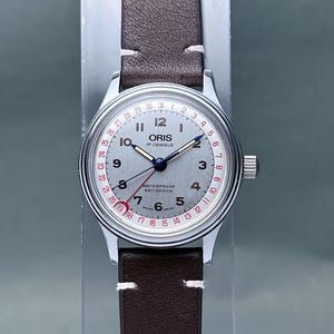 May include: A white ceramic mug with a black handle and the text "But First, Coffee" in a black, handwritten-style font. The mug is on a white surface.