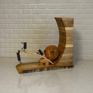 May include: A unique wooden sculpture featuring a curved, layered wooden structure with a large, round wooden element. Two small figures made of wood and metal appear to be interacting with the sculpture. The base is made of wood.