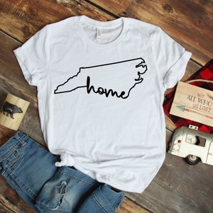 May include: White t-shirt with a black outline of the state of North Carolina and the word "home" written inside the outline.