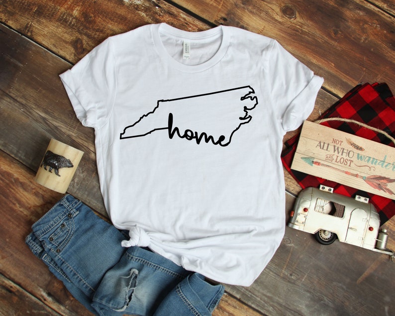 May include: White t-shirt with a black outline of the state of North Carolina and the word "home" written inside the outline.