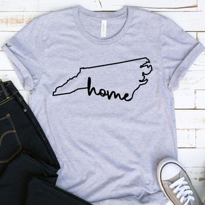 May include: Gray t-shirt with a black outline of the state of North Carolina and the word "home" written inside the outline.