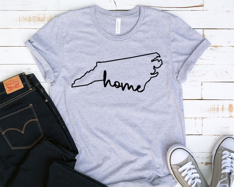May include: Gray t-shirt with a black outline of the state of North Carolina and the word "home" written inside the outline.